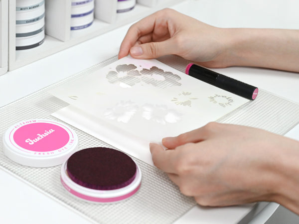 Secure the stencil over your cardstock with low-tack tape or a sticky mat.